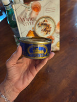 Hand holding a can of Cap'n Jim's Smoked Salmon over a magazine on a wooden surface