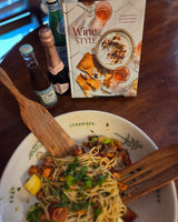 Plate of pasta with a book called Wine Styles, and bottles of wine on a wooden table