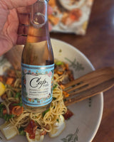 Bottle of Cava sparkling wine held over a bowl of pasta salad with a blurred background.